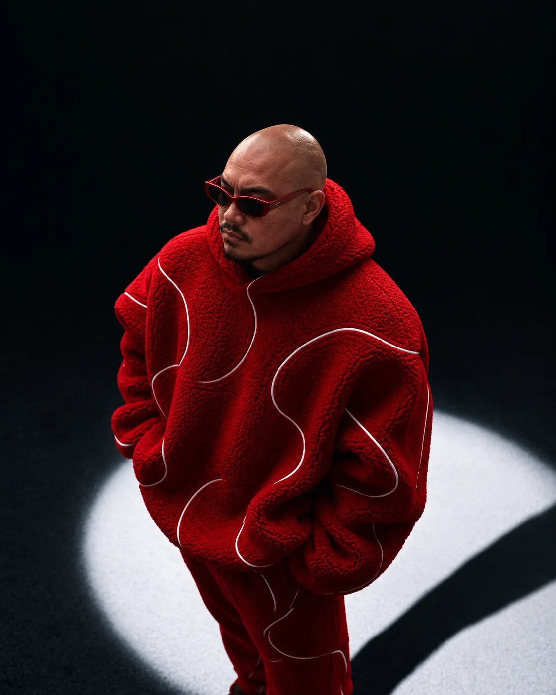Meka standing in a spotlight in the red sherpa set